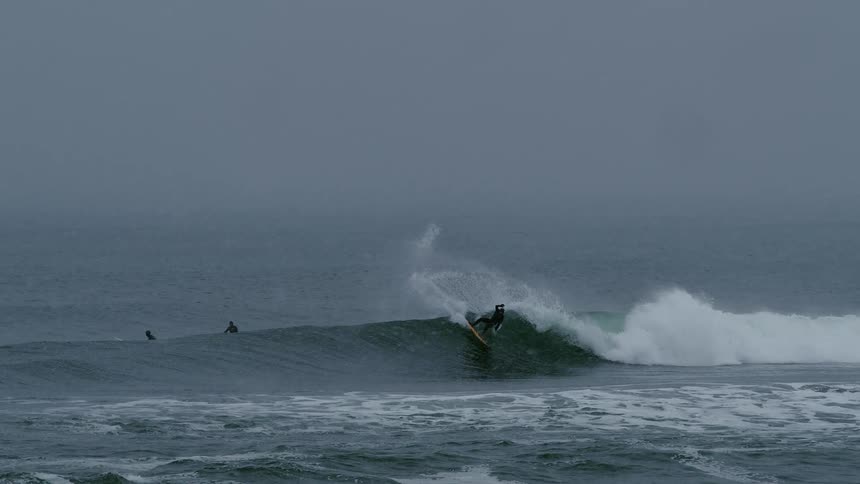 Surfers in the sea with one of them doing a maneuver on a wave on a snowy day