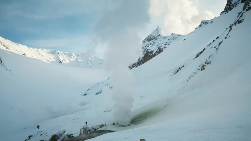 Steam rising from a hotspring in between a snowcapped mountain summit