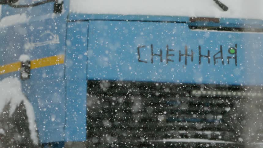 Snow falls in front of a blue bus