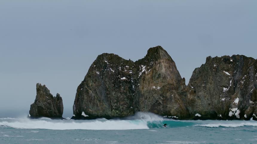 Surfer riding a big wave in the ocean with snowy rocks in the background