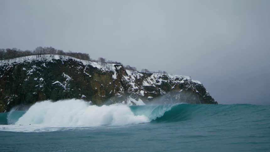 Big tube wave in the ocean with the snowy coast next to it