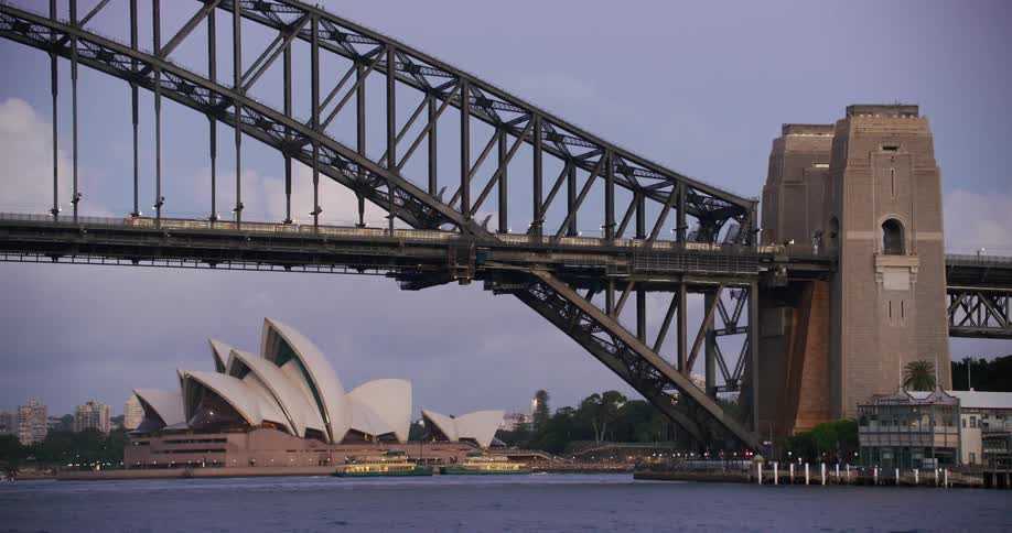 A bridge with a train passing by and ferry boats near an opera house in australia