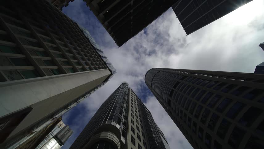 Upward view between buildings against a cloudy sky