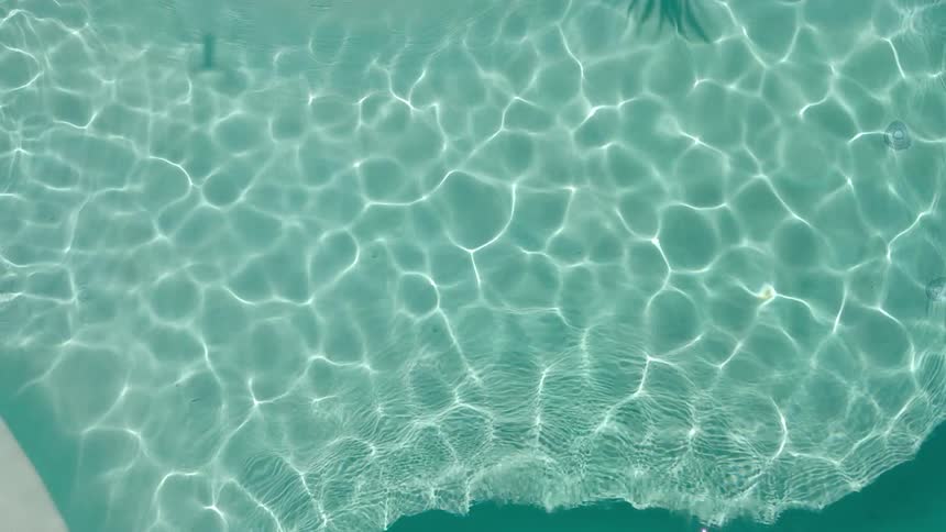 Top view of a crystal blue pool with sun reflection