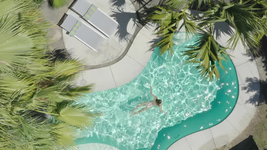 Aerial view of a woman swimming on a swimming pool with clear blue water