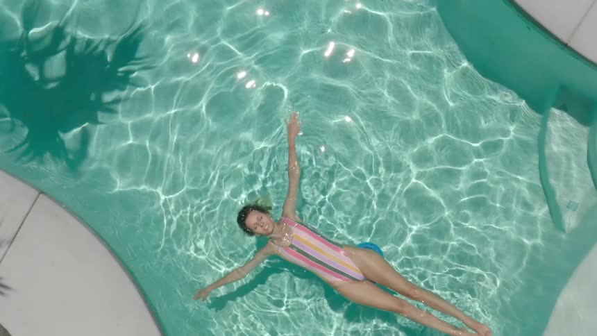 A woman in a one piece swim suit floats in a pool with her arms and legs extended
