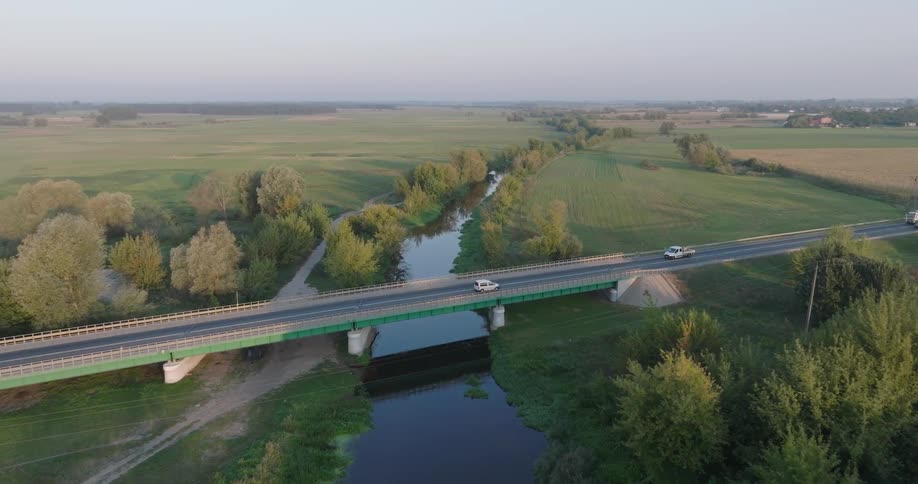 Vehicles drive over the bridge crossing the stream