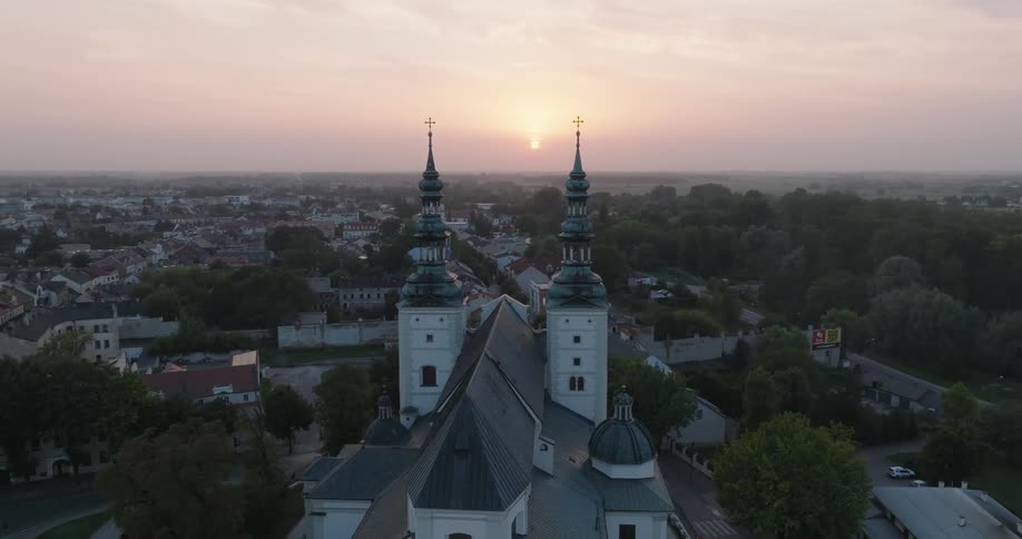 A majestic cathedral stands tall against a sunrise over a small town cityscape
