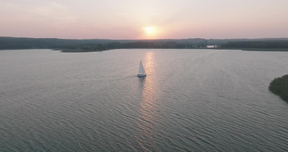 A single sailboat on a vast body of water with the sun setting near the horizon