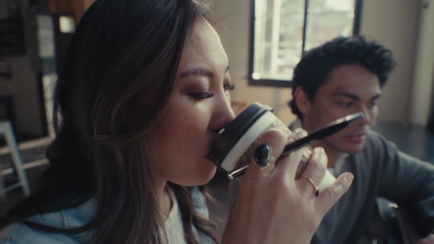 A young woman drinking from a disposable cup and a man in her side is talking to her
