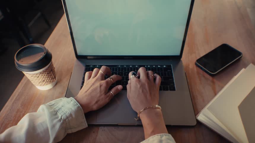 An adult sits at a wooden table while typing on a laptop