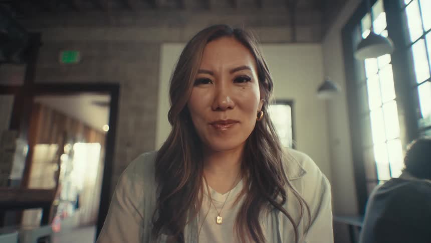 An asian woman at work smiles as she focuses on her computer screen