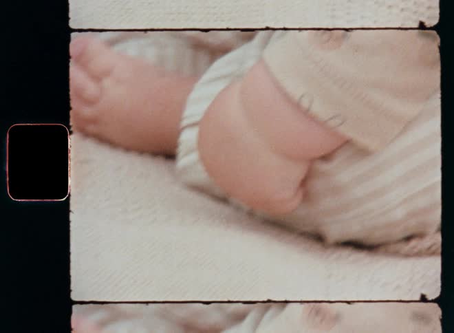Close up Super 8 shots of a baby’s hands feet and legs while sitting outdoors on a carpet or picnic blanket feeling the soft beige fabric and touching it with the tiny fingers full of playful curiosity