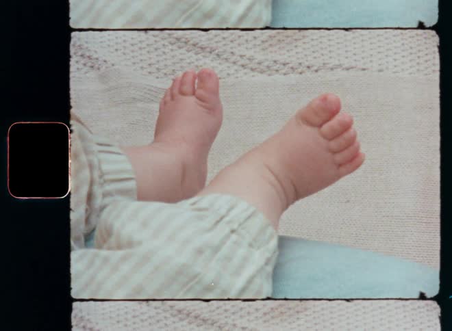 Vintage Super 8mm close-up of a white Caucasian baby’s feet sleeping or resting on the mother’s lap as symbol for parenthood and trust and a happy and careless childhood with a nostalgic feeling or vibe