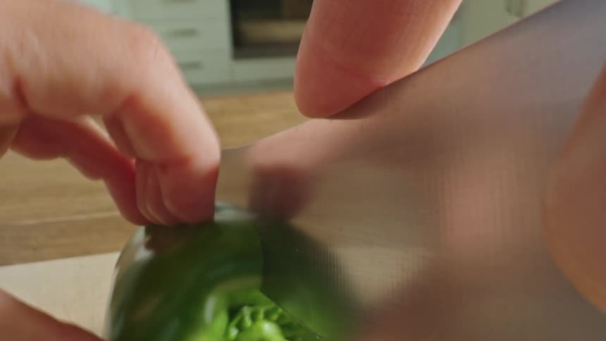 Point of view of a hand with a knife cutting a green pepper