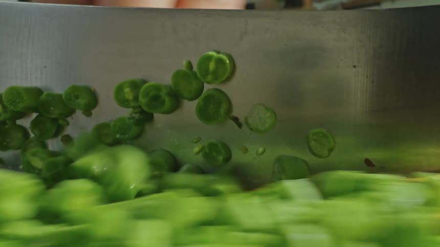 Point of view of a knife cutting green vegetables