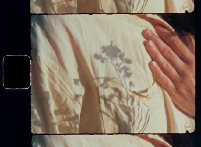 A shadow of a beautiful pink fireweed flower moves across the chest of a smiling brunette women touching her own body at her heart covered in soft linen fabric or shirt with her hand expressing self-love and happiness with avant-garde or hip fashion vibe