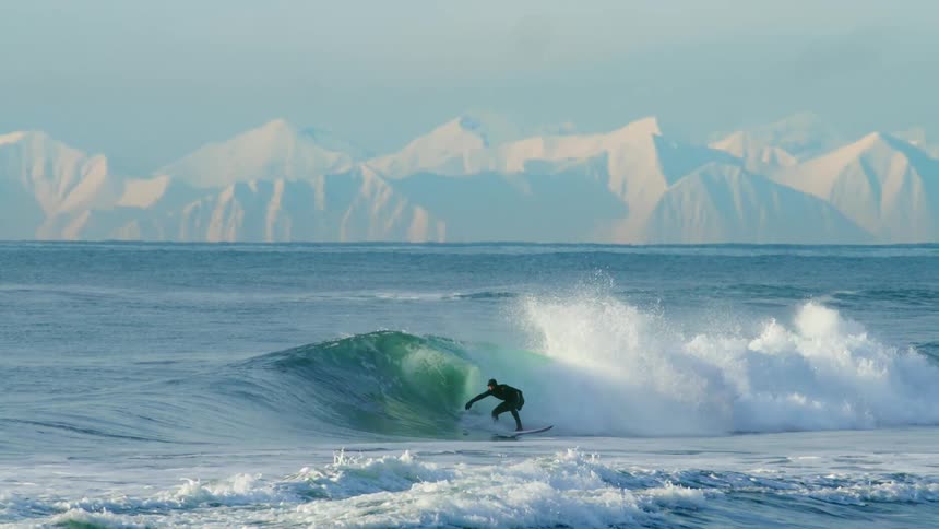 Person doing tricks on a wave with snowcovered mountains in the background