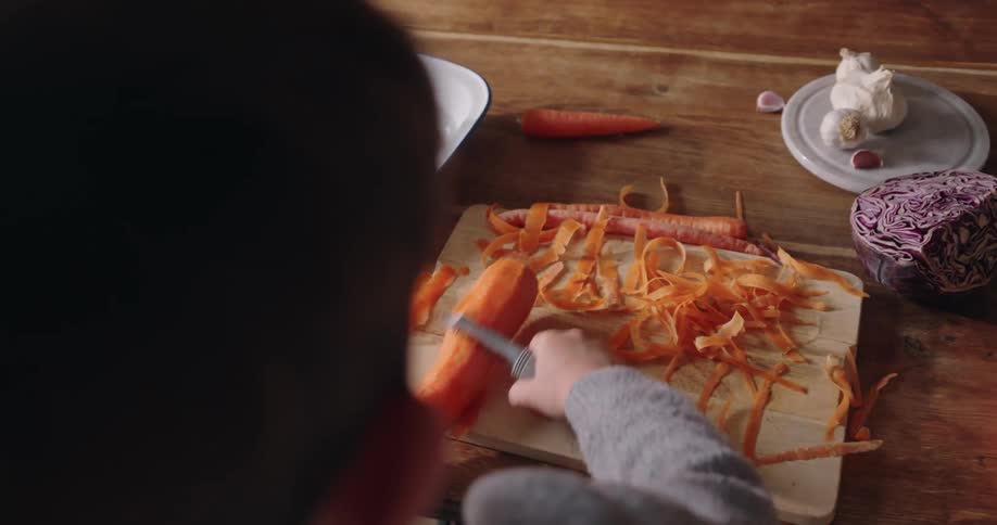 A child is peeling a large carrot