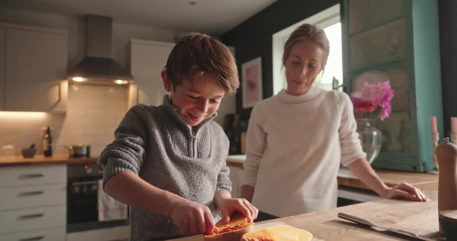 A mother watches her son clean a butternut squash but becomes concerned when he threatens to flick some on her with a spoon