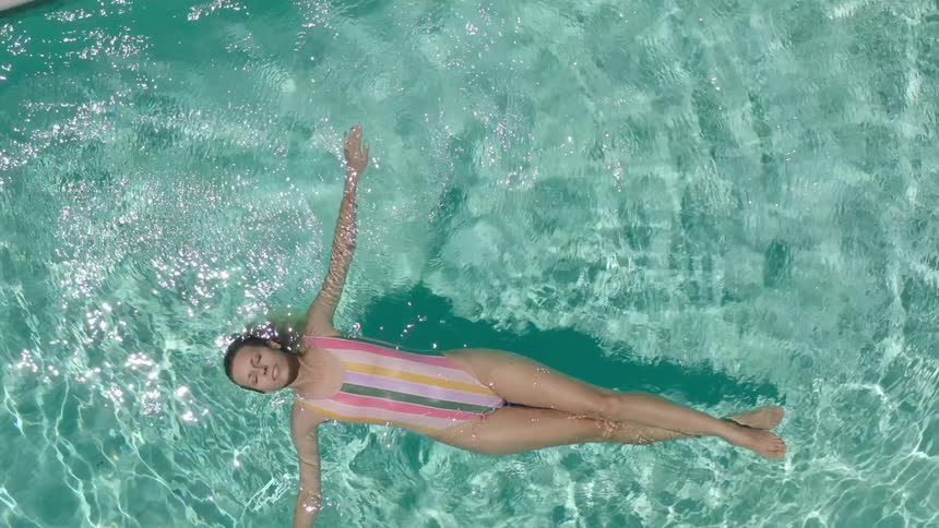 Aerial of a woman in striped swimsuit floating in a pool