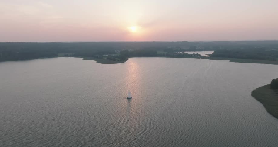 A single sailboat on a vast lake with a setting sun on the horizon