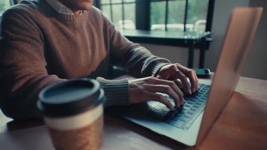 A man looks slightly stressed while reading and typing on a laptop in an office