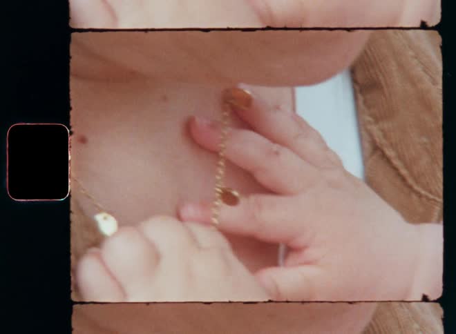 Closeup of a baby’s small hands holding or playing with the golden necklace on the mother’s neck expressing curiosity and love for the caring parent while caressing or touching her skin on heartwarming vintage 8mm film footage