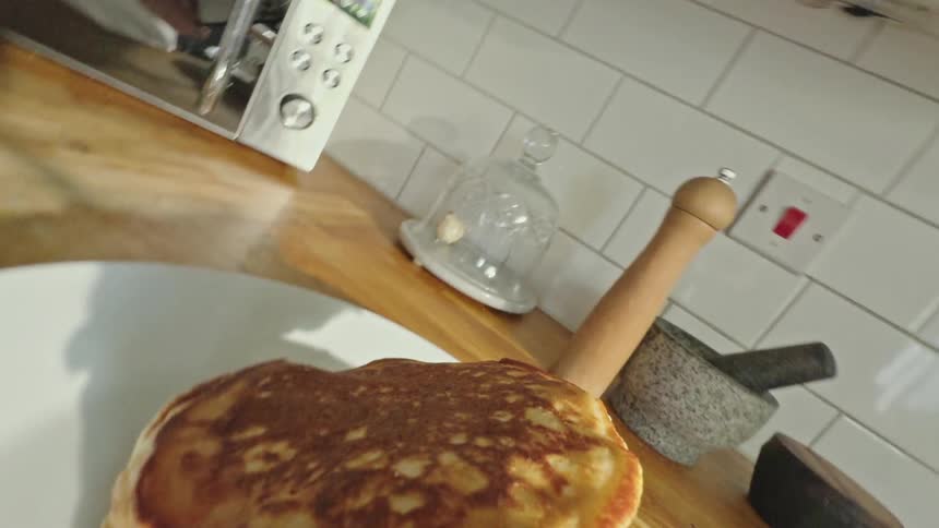 Point of view shot of a spatula picking up a pancake from a pan and placing it on a plate