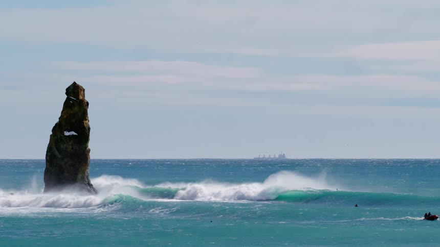 A large rock formation protruding from the ocean with waves breaking around it