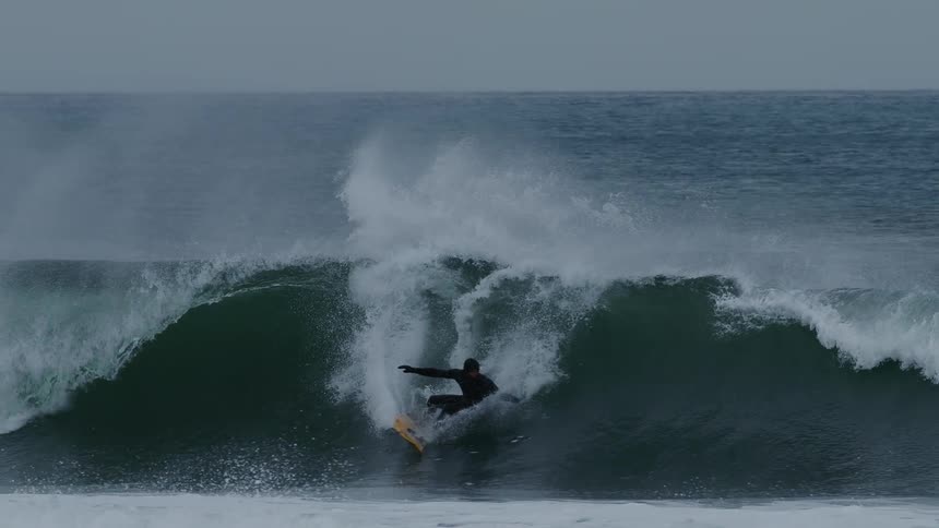 A male surfer rides a wave off of a coast during winter