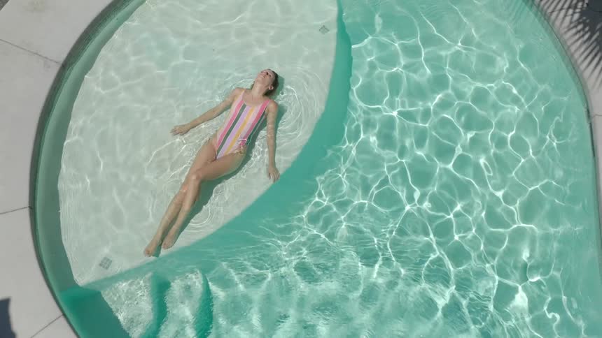 Woman in swimsuit lying in pool with sun reflection
