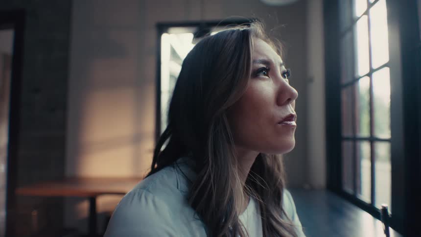A contemplative woman sitting at a cafeteria window holding a pen