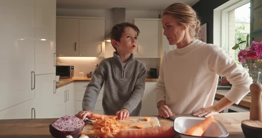 Boy and his mother in the kitchen tasting a carrot and cooking together