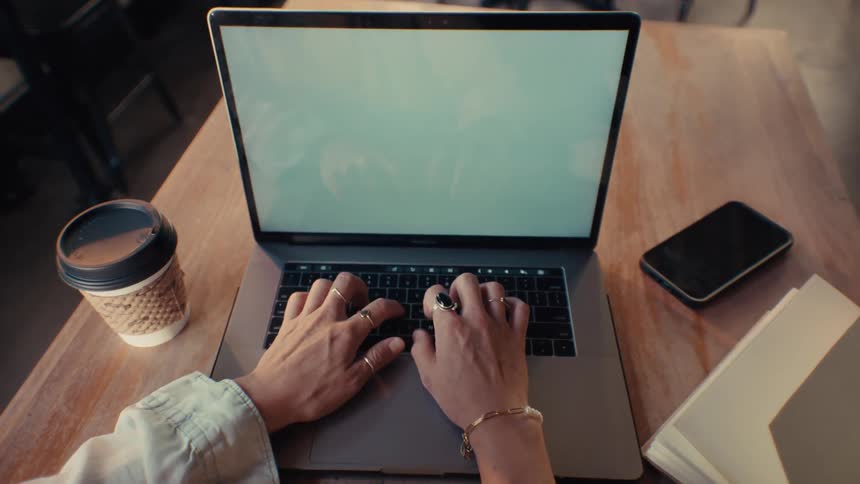 Pov of a womans hands typing on a laptop and then picking up her smartphone next to her