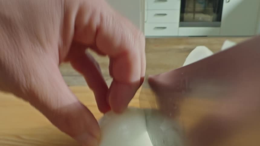 A person uses a large knife to cut a white onion in a kitchen