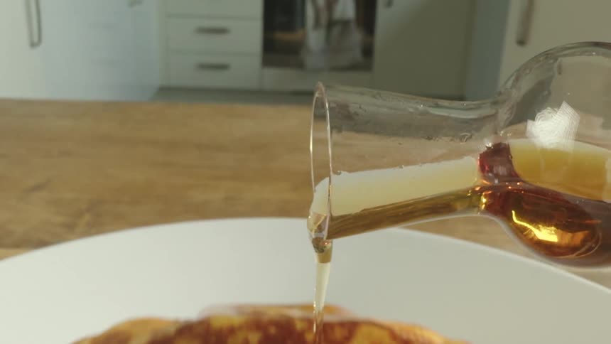 Poring maple syrup over pancakes