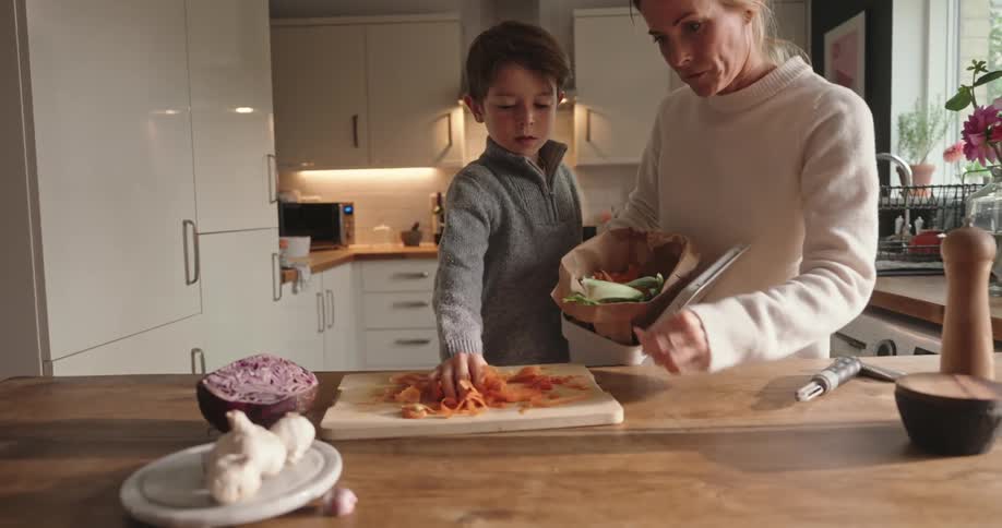 A woman and a child in a kitchen picking up garbage left over from preparing food and throwing it in the trash bin
