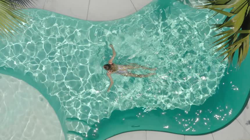 Overhead view of a woman swimming across a sparkling swimming pool