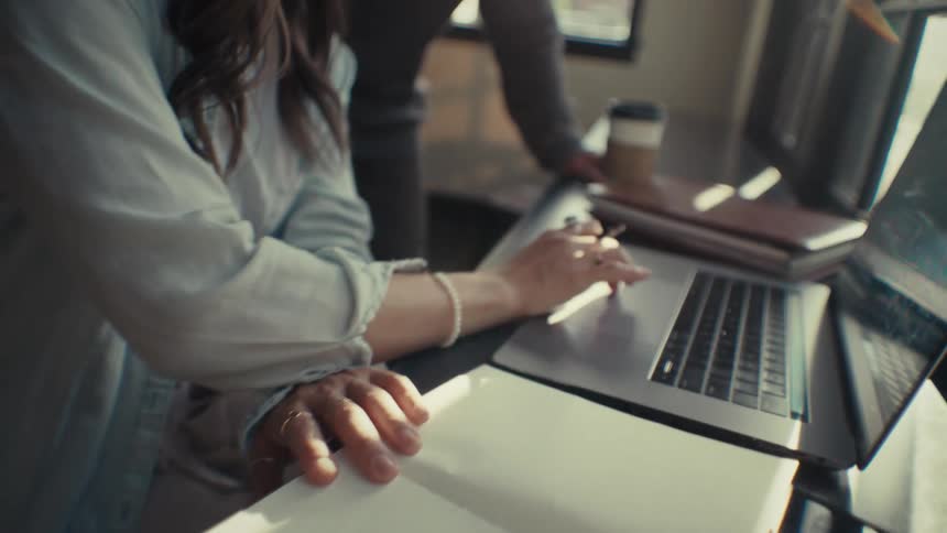 Hands of a woman writing in a book and typing on a laptop
