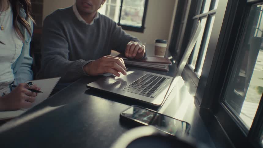 Two coworkers seated at a table with a laptop and a smartphone in front of them