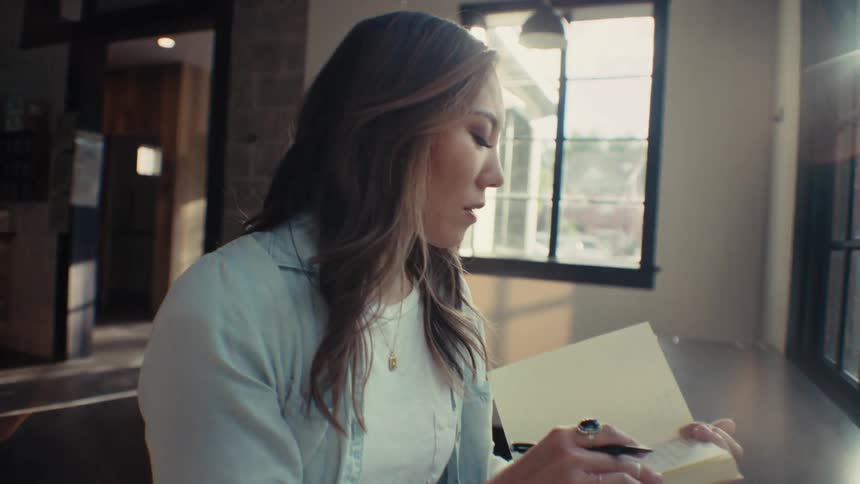 An asian woman looks through a book and checks something on a laptop in an office