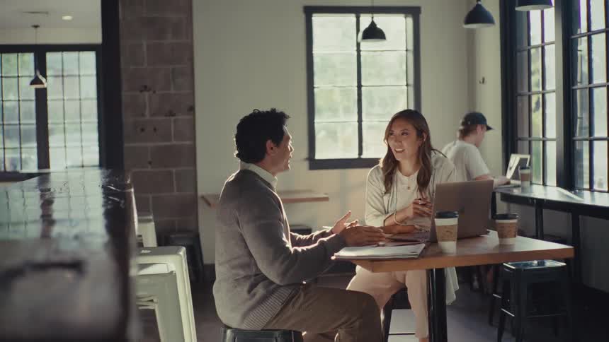 Two individuals seated at a table in a coffee shop engaged in conversation