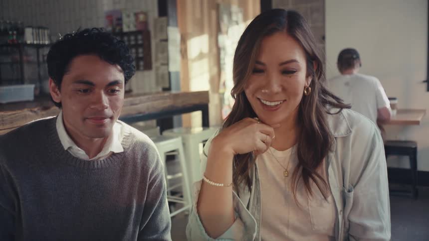 Two employees in an office smile and talk while looking at a laptop screen