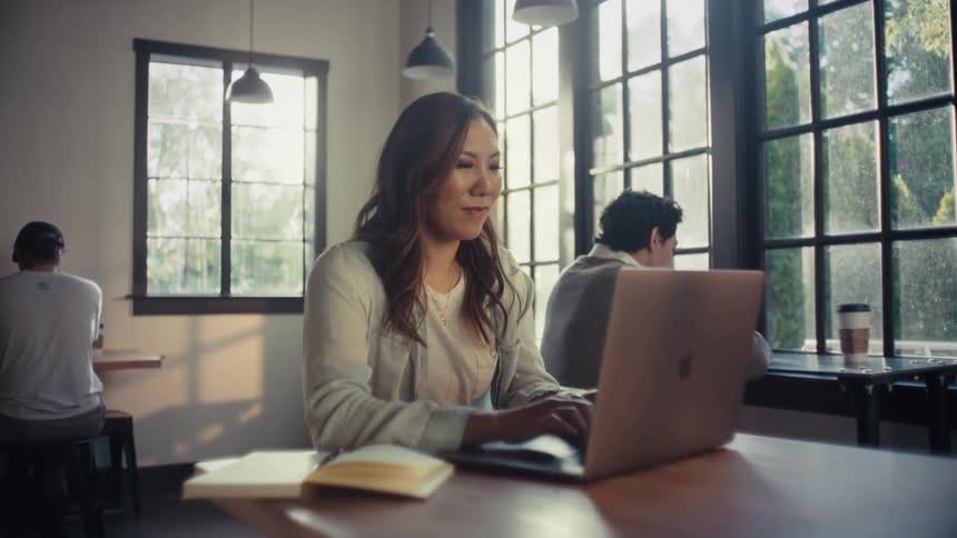 Asian Woman sitting typing on a laptop in a coffee shop