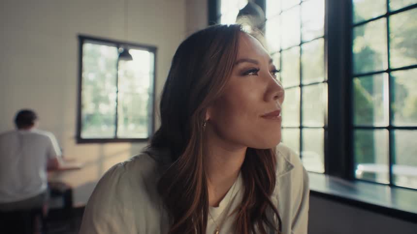 Closeup of a woman with long hair sitting indoors looking up with a smile