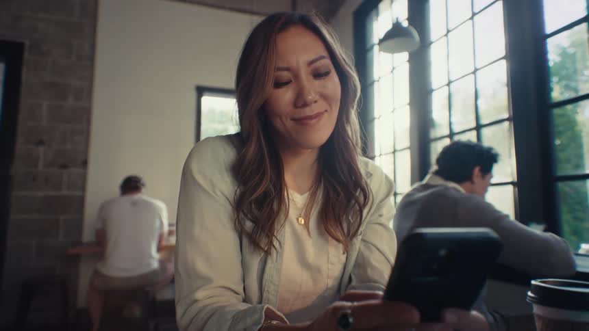 An asian employee in an office smiles as she texts on her smartphone