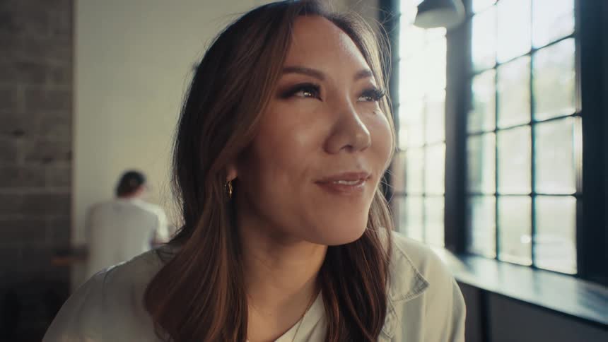 Closeup of a woman with long hair sitting indoors looking up with a smile