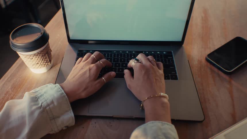 Hands of a woman typing on a laptop on a wooden table