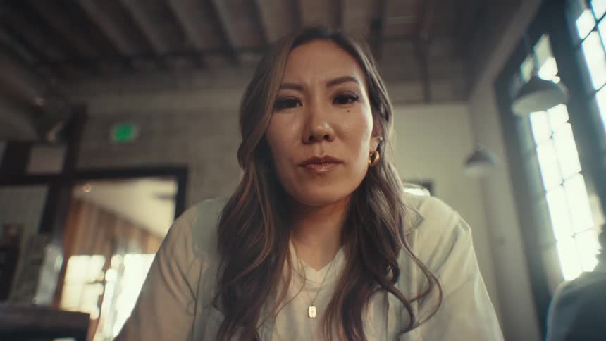 A woman with long hair and a white top looks intently at the camera